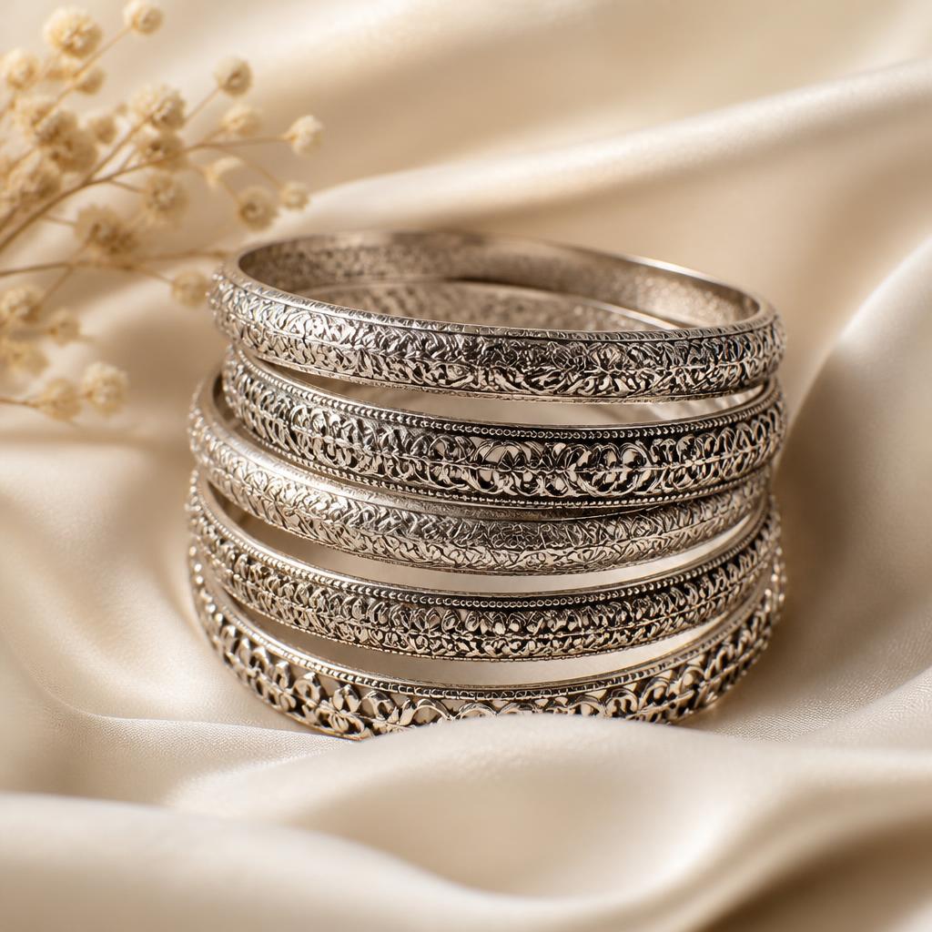 Stack of hand-engraved sterling silver filigree bangles on ivory silk